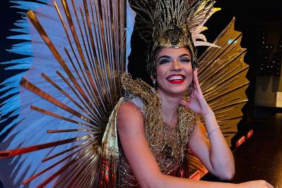 Personne portant un costume élaboré avec des ailes et un masque argenté, dans un décor intérieur faiblement éclairé.