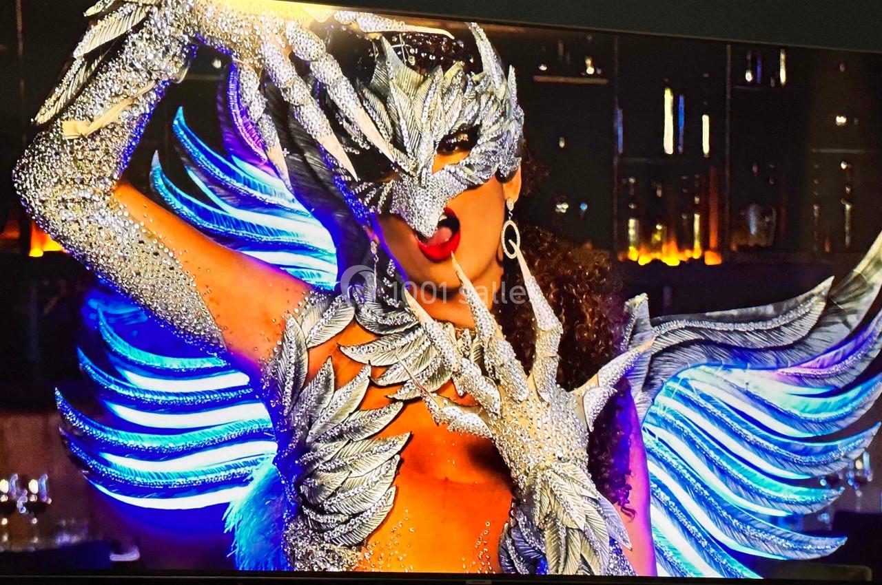 Personne portant un costume élaboré avec des ailes et un masque argenté, dans un décor intérieur faiblement éclairé.