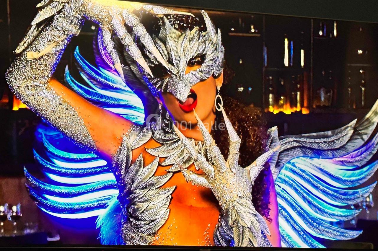 Personne portant un costume argenté étincelant avec des ailes et un masque élaboré, posant dans un décor sombre.