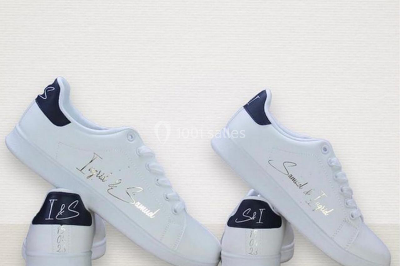 Chaussures blanches avec détails personnalisés en écriture argentée et talons bleu marine, posées sur une surface claire.