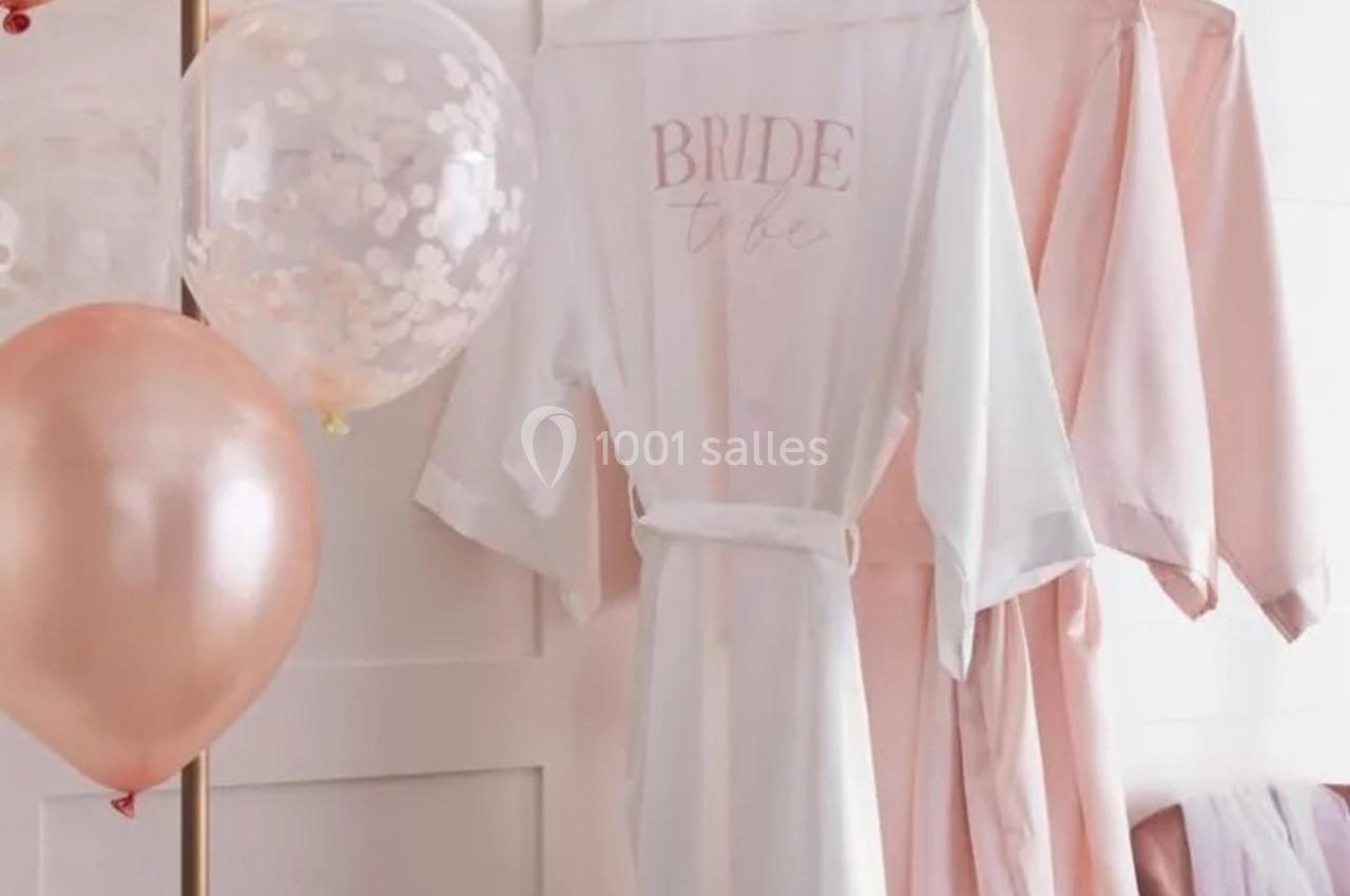 Peignoirs suspendus, dont un blanc avec l'inscription ’Bride to be’, entourés de ballons roses et blancs.