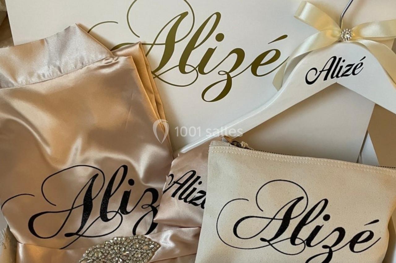 Ensemble d'articles personnalisés en satin beige, comprenant un cintre, une pochette et un tissu, avec le nom ’Alizé’.