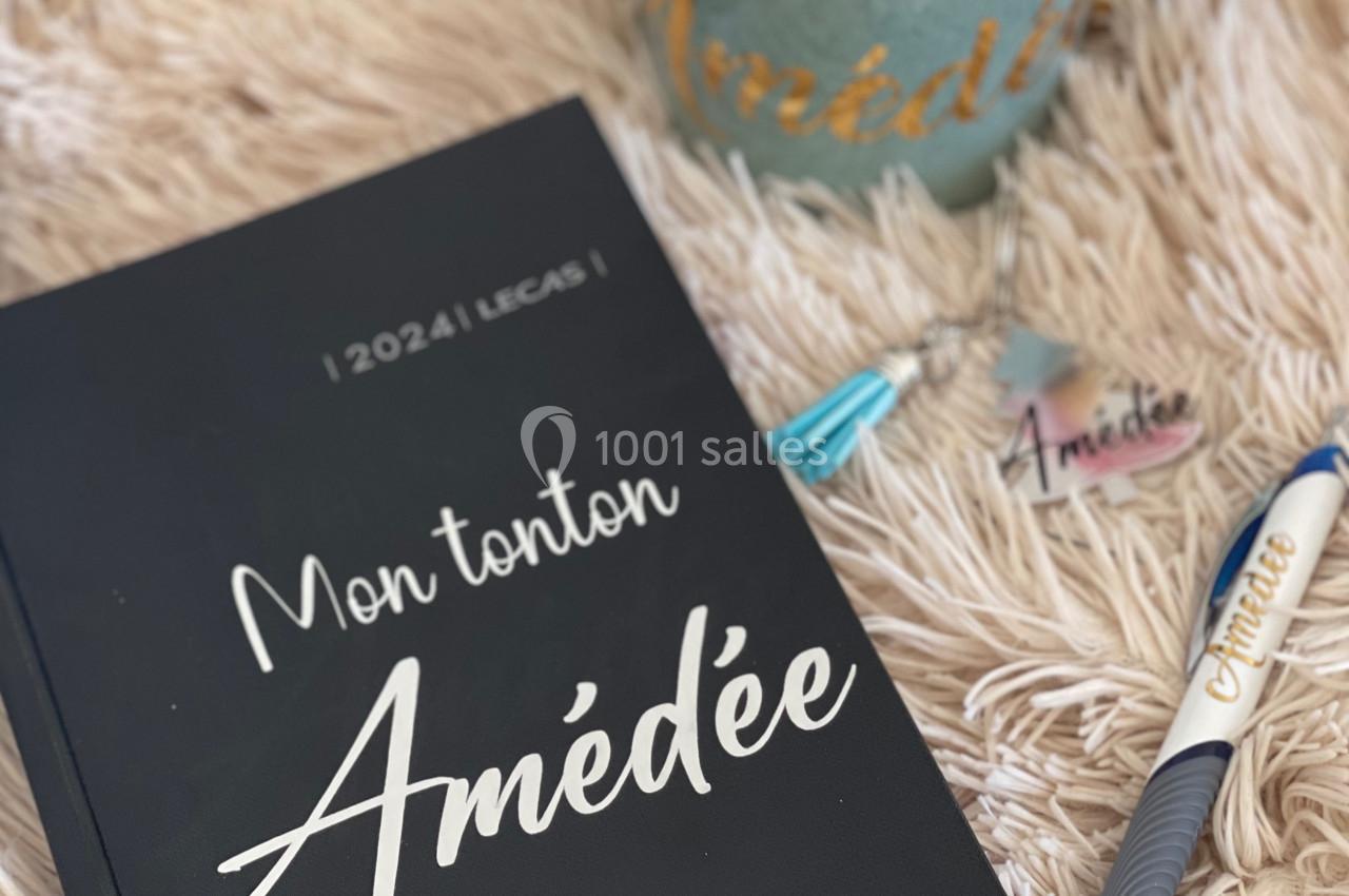 Carnet noir ’Mon tonton Amédée 2024’ posé sur un plaid beige, avec une tasse contenant des chocolats et un stylo.