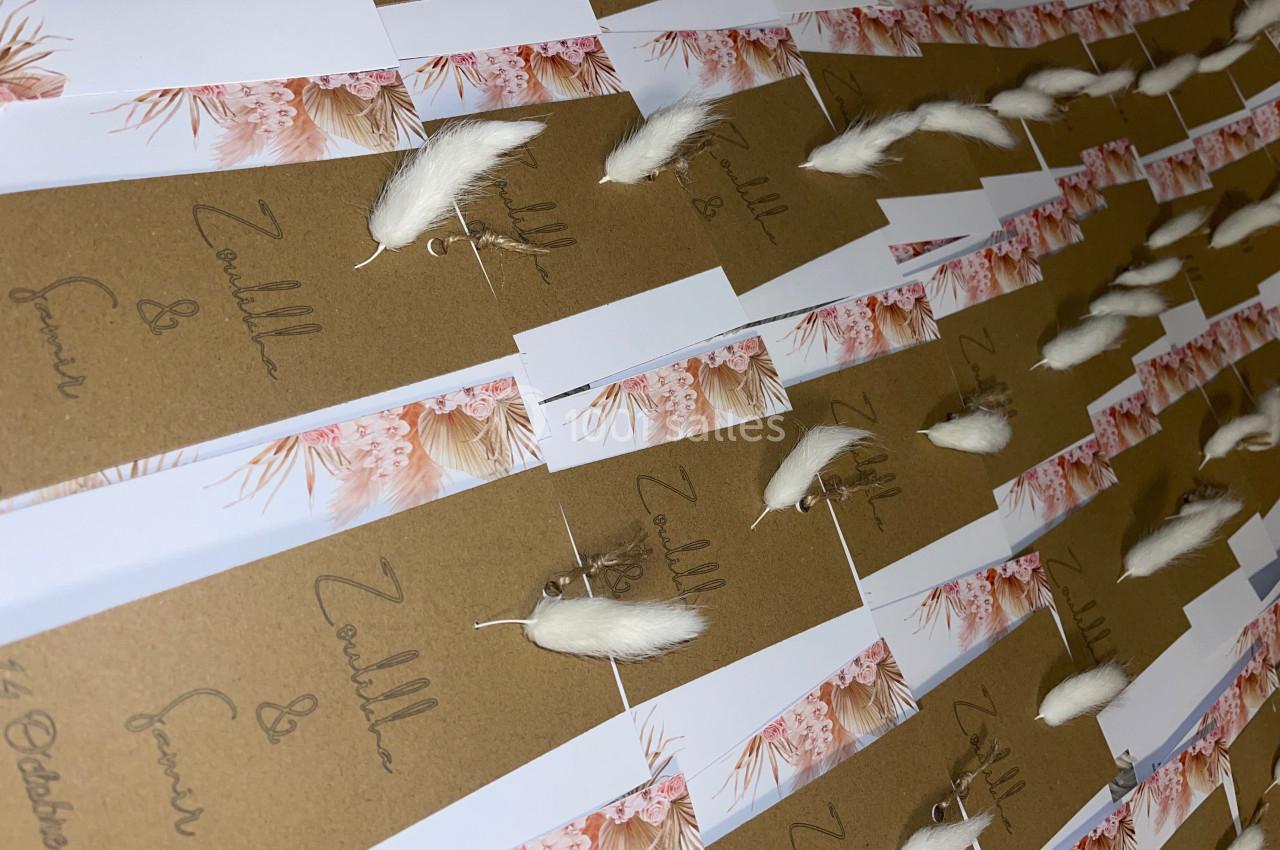 Cartes en papier kraft décorées de fleurs séchées blanches et roses, alignées sur une surface plane.