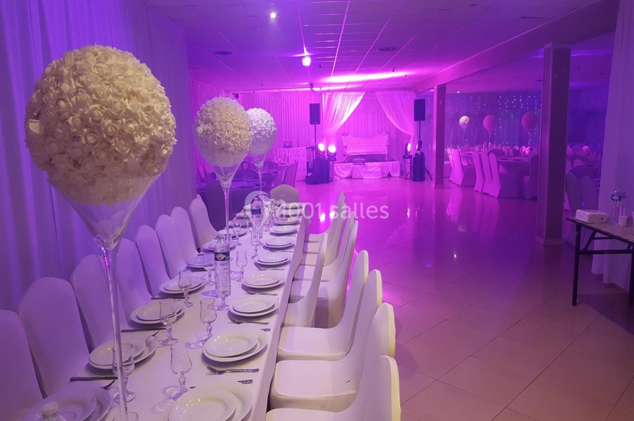 Salle de réception décorée avec des tables dressées, des chaises blanches et des centres de table en fleurs blanches.