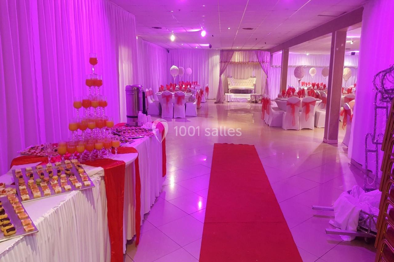 Salle de réception décorée en blanc et rouge avec tables dressées, buffet de desserts et éclairage violet.