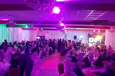 Plusieurs personnes discutent devant un bâtiment avec des voitures garées, dont une voiture rouge sportive.