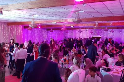 Plusieurs personnes discutent devant un bâtiment avec des voitures garées, dont une voiture rouge sportive.