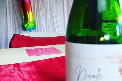 Ballon arc-en-ciel en forme de chiffre un, table décorée avec nappe rouge et bouteille au premier plan.