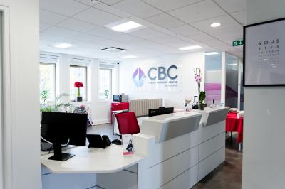 Salle de formation lumineuse avec tables blanches, chaises noires et grandes fenêtres laissant entrer la lumière naturelle.