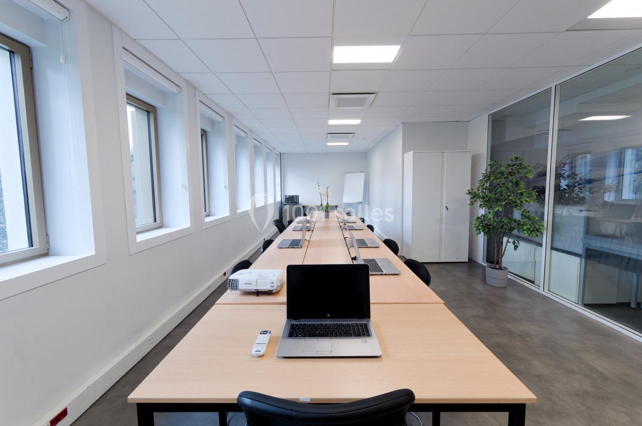 Salle de réunion lumineuse avec une grande table, des ordinateurs portables, un projecteur et des chaises.