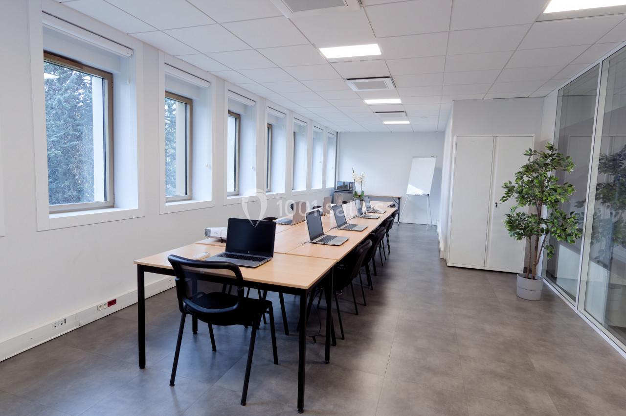 Salle de réunion lumineuse avec une longue table, des chaises, des ordinateurs portables et un tableau blanc.