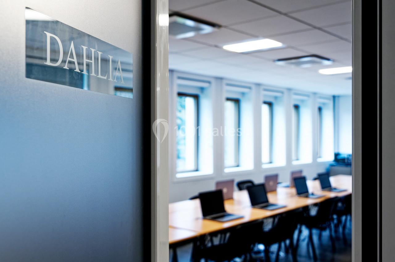 Salle de réunion lumineuse avec une grande table en bois et des chaises noires, vue à travers une porte entrouverte.