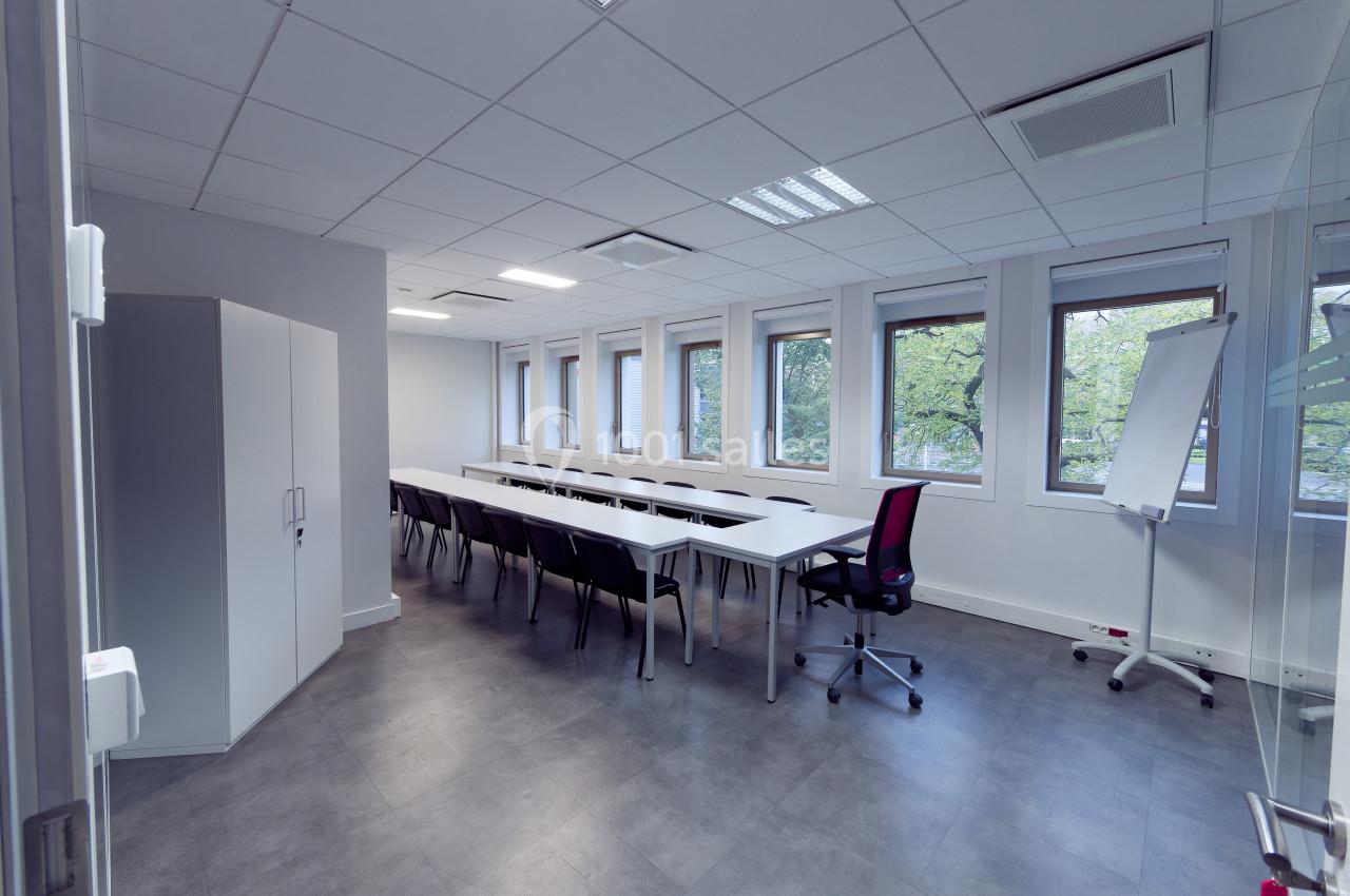 Salle de réunion lumineuse avec une grande table, des chaises noires, un tableau blanc et des fenêtres donnant sur des…