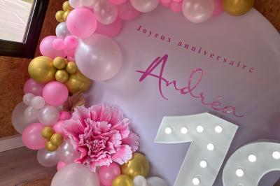 Décoration d'anniversaire avec ballons violets et blancs, chiffre lumineux ’18’ et présentoirs cylindriques blancs.