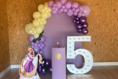 Décoration d'anniversaire avec ballons violets et blancs, chiffre lumineux ’18’ et présentoirs cylindriques blancs.