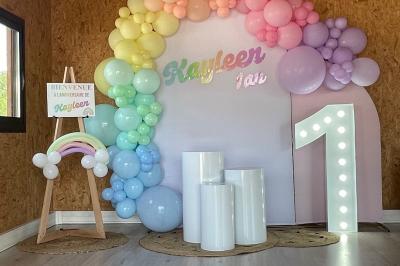 Décoration d'anniversaire avec ballons violets et blancs, chiffre lumineux ’18’ et présentoirs cylindriques blancs.