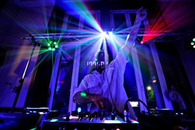 Un homme en costume utilise une table de mixage lors d'un événement en extérieur, avec des ballons en arrière-plan.
