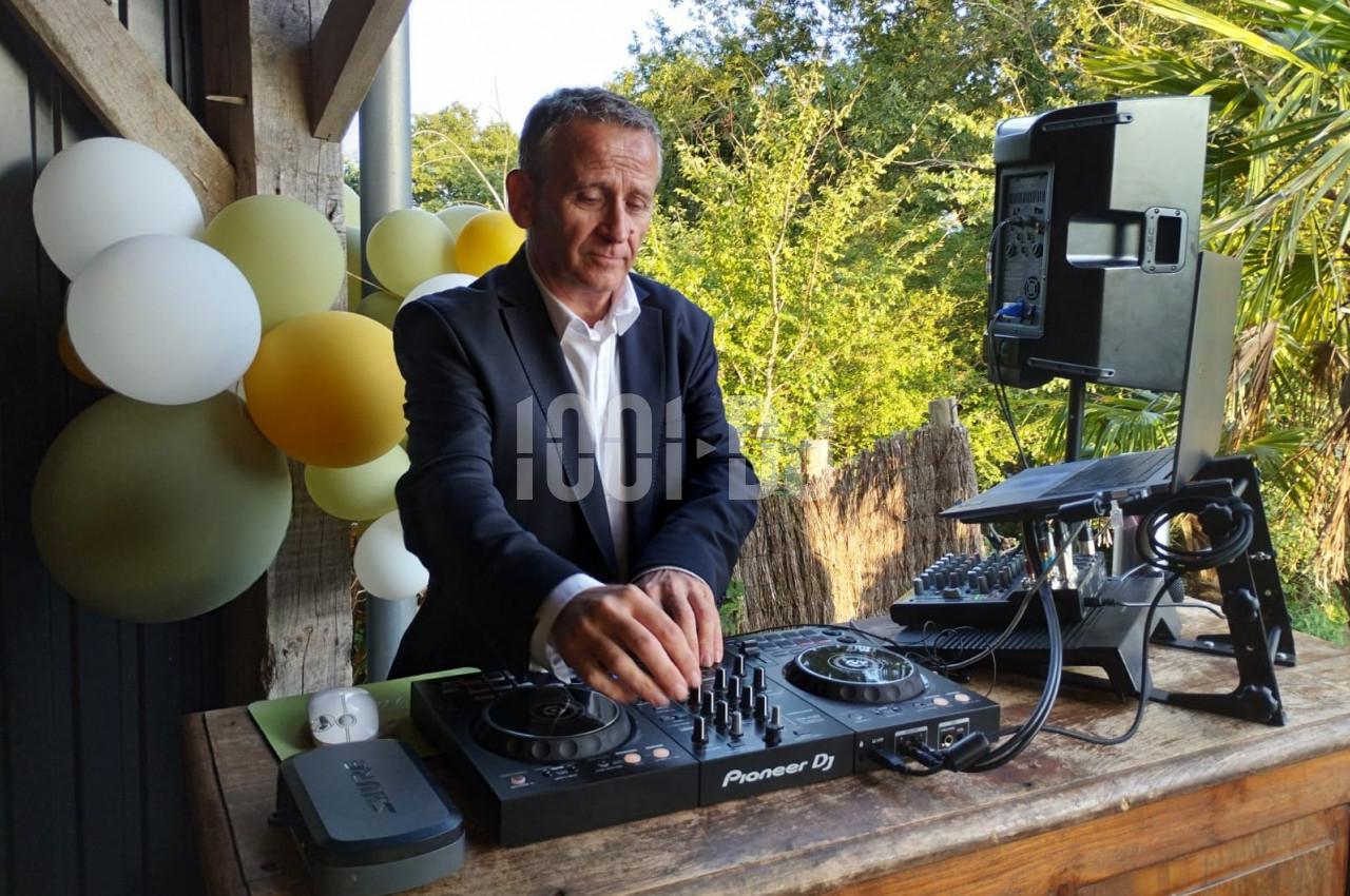 Un homme en costume utilise une table de mixage lors d'un événement en extérieur, avec des ballons en arrière-plan.