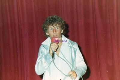 Un homme en costume utilise une table de mixage lors d'un événement en extérieur, avec des ballons en arrière-plan.