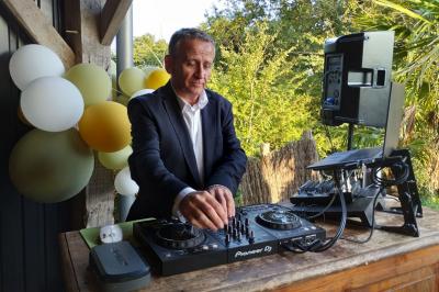 Un homme en costume utilise une table de mixage lors d'un événement en extérieur, avec des ballons en arrière-plan.