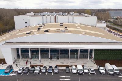 Miniature Location salle Croissy-Beaubourg (Seine-et-Marne) - La Mega Place #29 Vue aérienne d'un grand bâtiment moderne avec un parking rempli de voitures à l'avant et des arbres en arrière-plan.