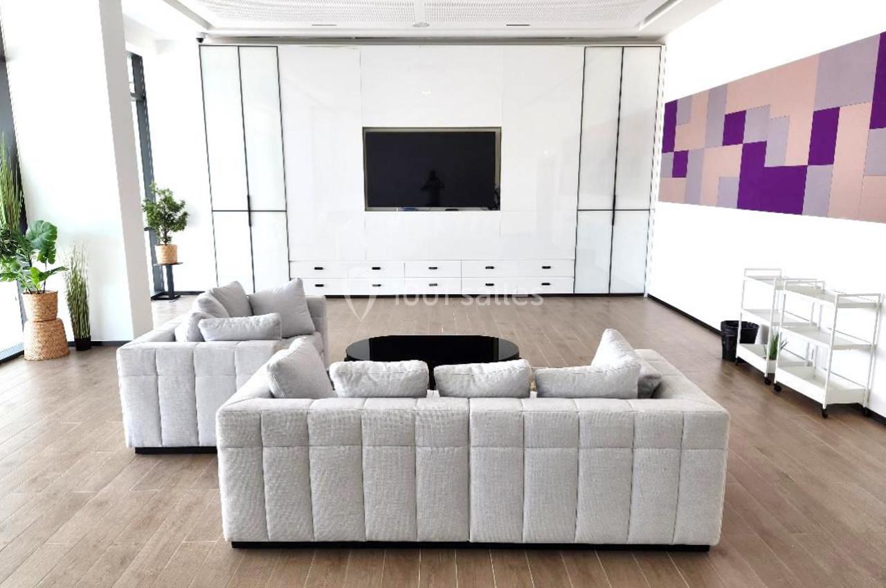 Salon moderne avec deux canapés gris, table basse noire, écran mural et décoration murale géométrique colorée.