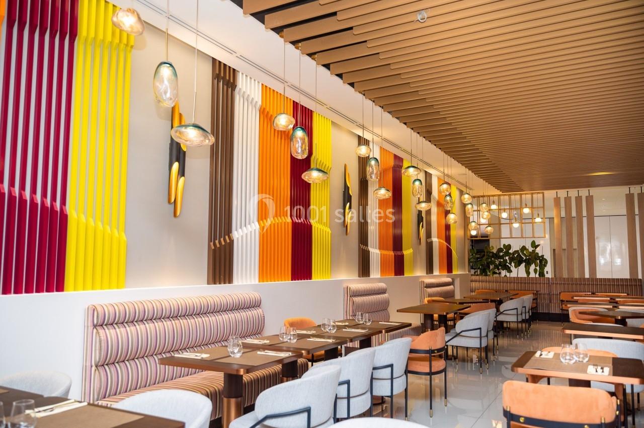 Salle de restaurant moderne avec banquettes rayées, chaises rembourrées, luminaires suspendus et murs colorés.