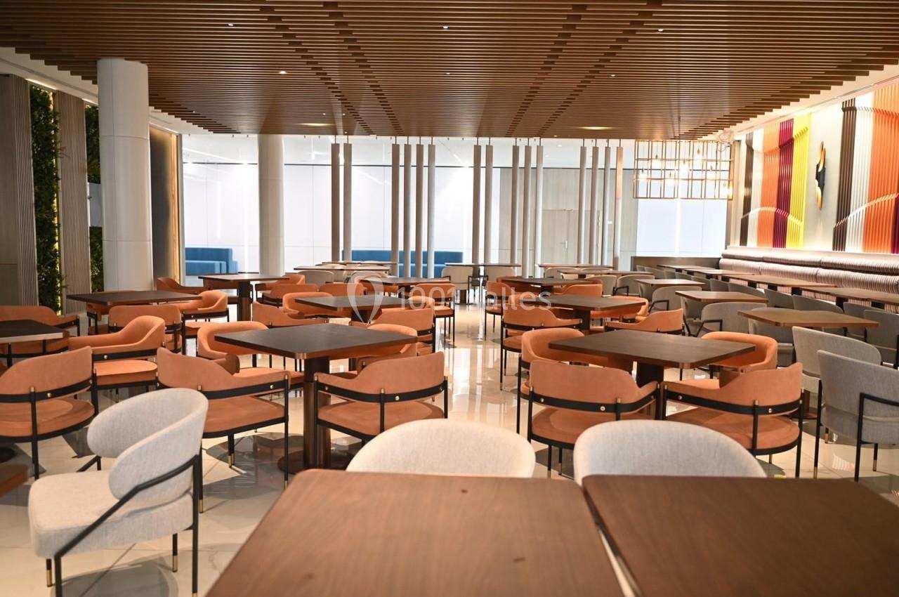 Salle de restaurant moderne avec des tables en bois, des chaises rembourrées et un éclairage naturel.
