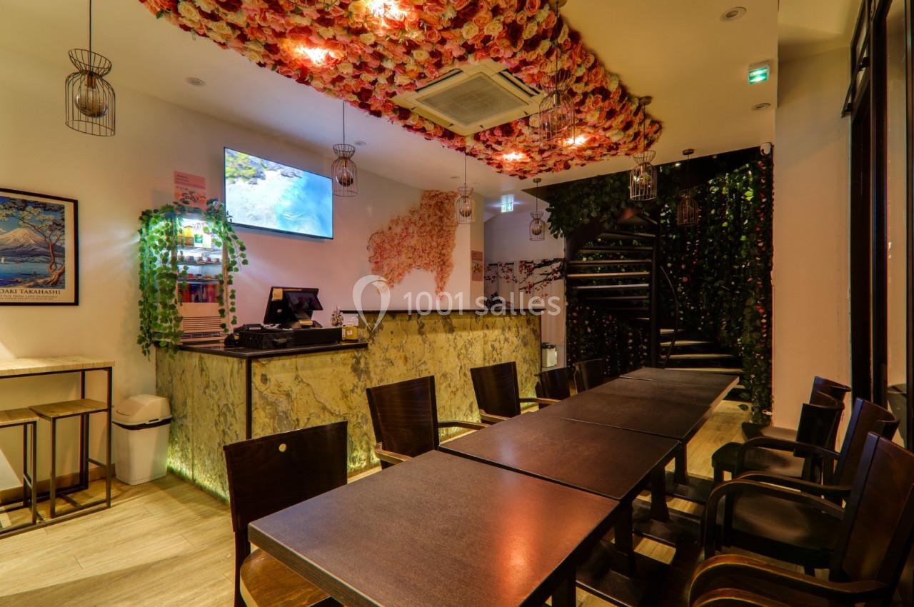 Intérieur d'un restaurant avec plafond décoré de fleurs, comptoir en marbre, tables en bois et escalier au fond.