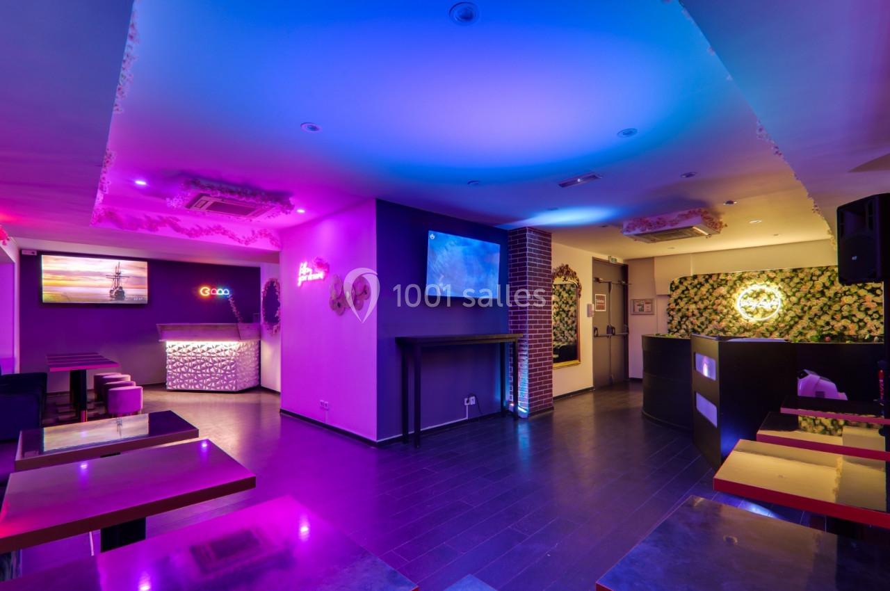 Salle moderne avec éclairage coloré, tables, bar lumineux et écrans muraux dans un décor contemporain.