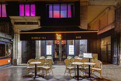 Façade d'un bar à bubble tea avec terrasse extérieure, tables et chaises en osier, éclairage nocturne.