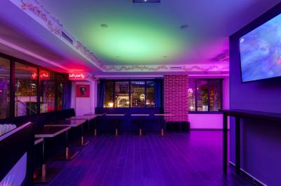 Salle lumineuse avec éclairage coloré, banquettes noires, tables en bois et grandes fenêtres donnant sur l'extérieur.