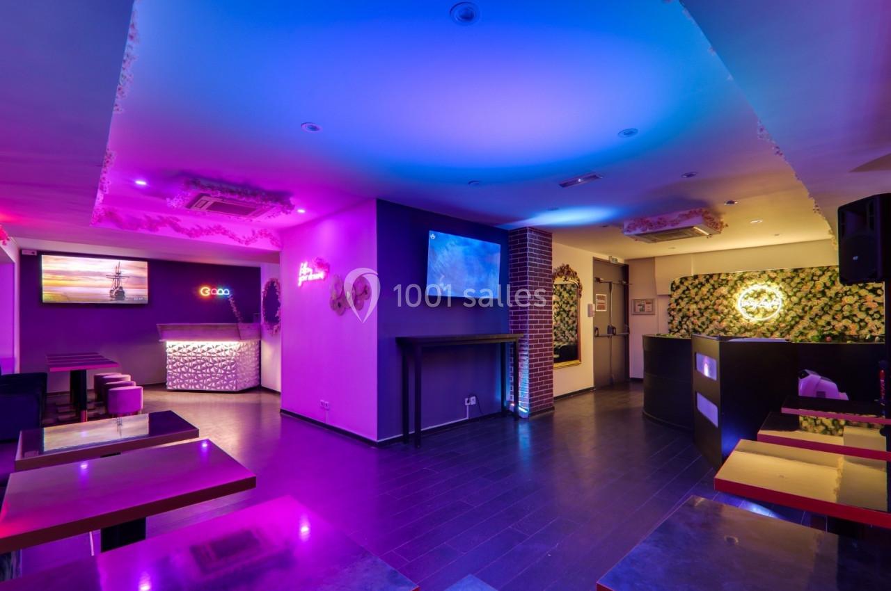 Salle moderne avec éclairage coloré, tables et comptoir, décorations murales et écran lumineux.