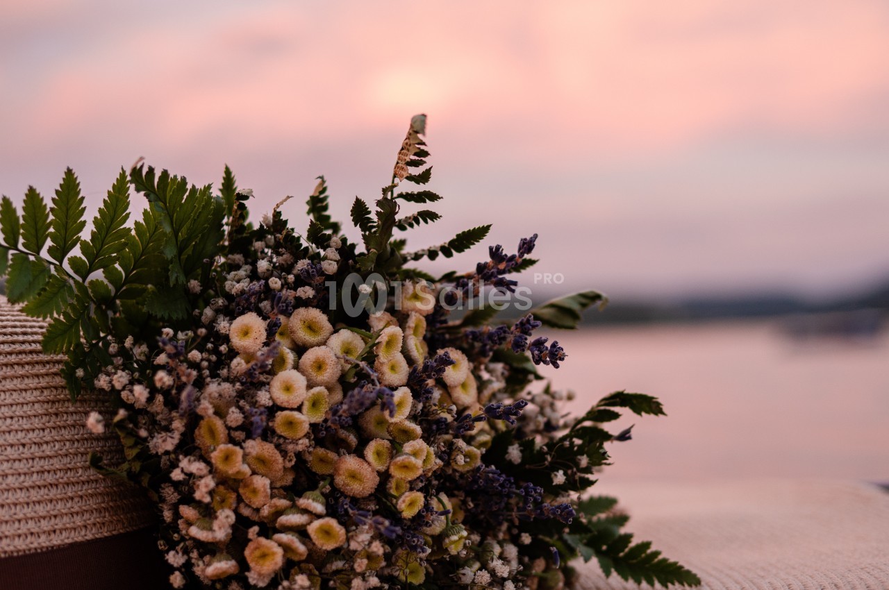 Bouquet de fleurs sauvages posé sur un chapeau en paille, avec un coucher de soleil flou en arrière-plan.