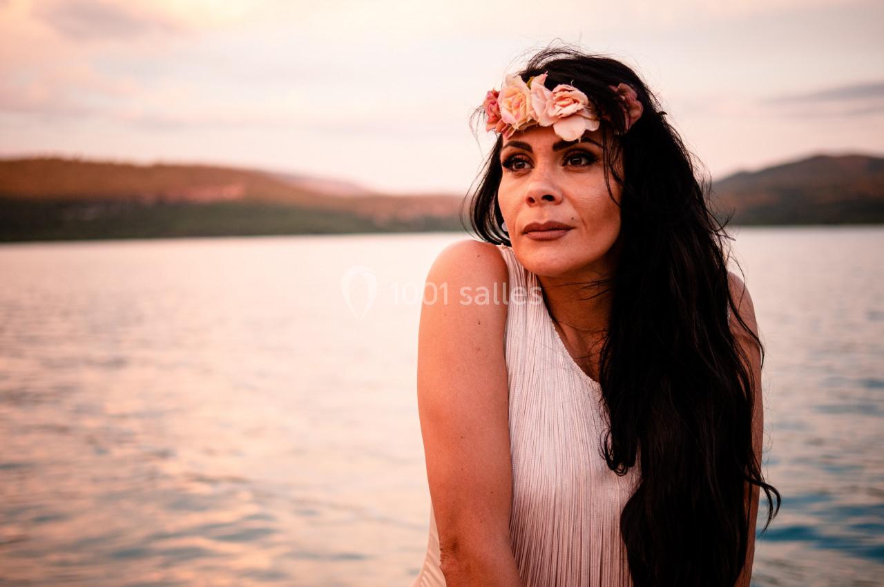 Femme portant une couronne de fleurs, regardant au loin devant un lac au coucher du soleil.