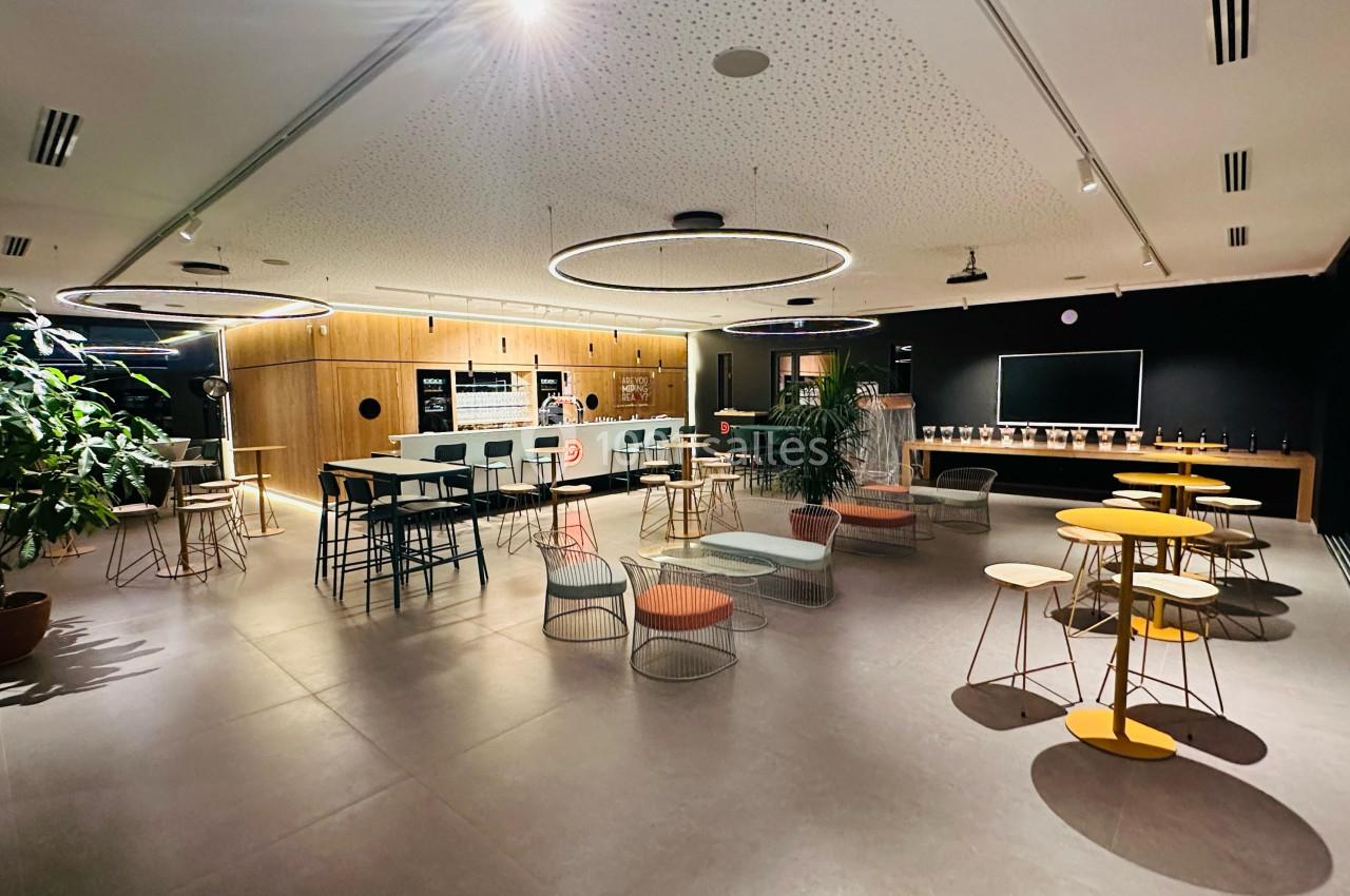 Salle moderne avec tables, chaises colorées, plantes et éclairage circulaire, aménagée pour des pauses ou réunions…