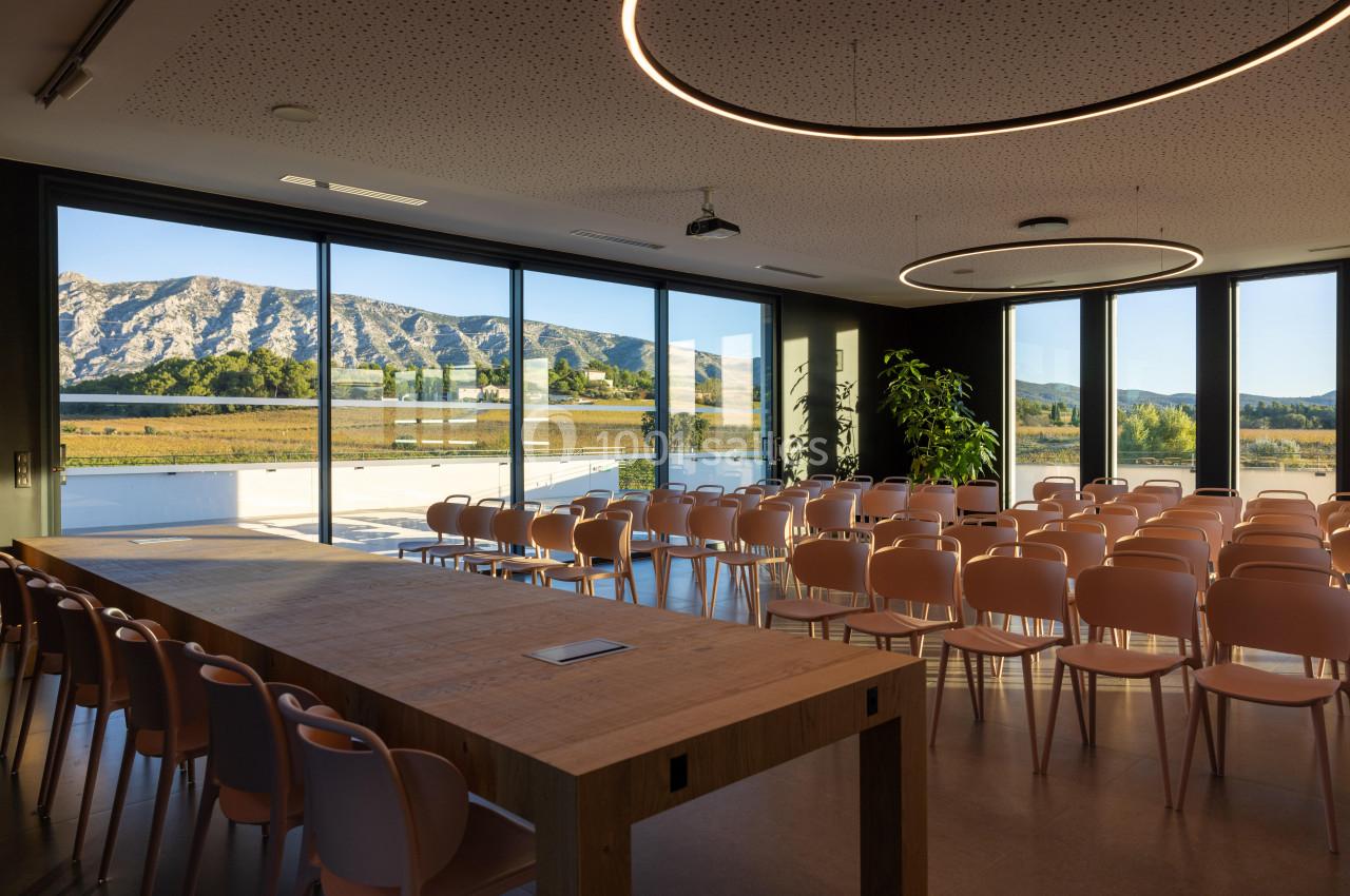 Salle de conférence lumineuse avec des chaises alignées, une grande table en bois et vue sur un paysage montagneux.