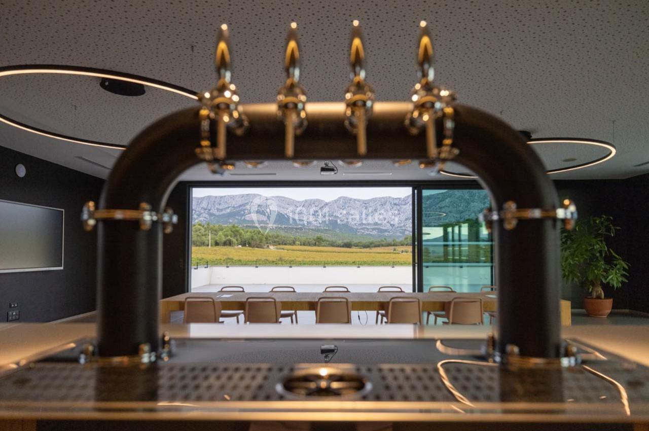 Robinet de bar en premier plan avec vue sur une salle moderne et un paysage montagneux à travers une baie vitrée.
