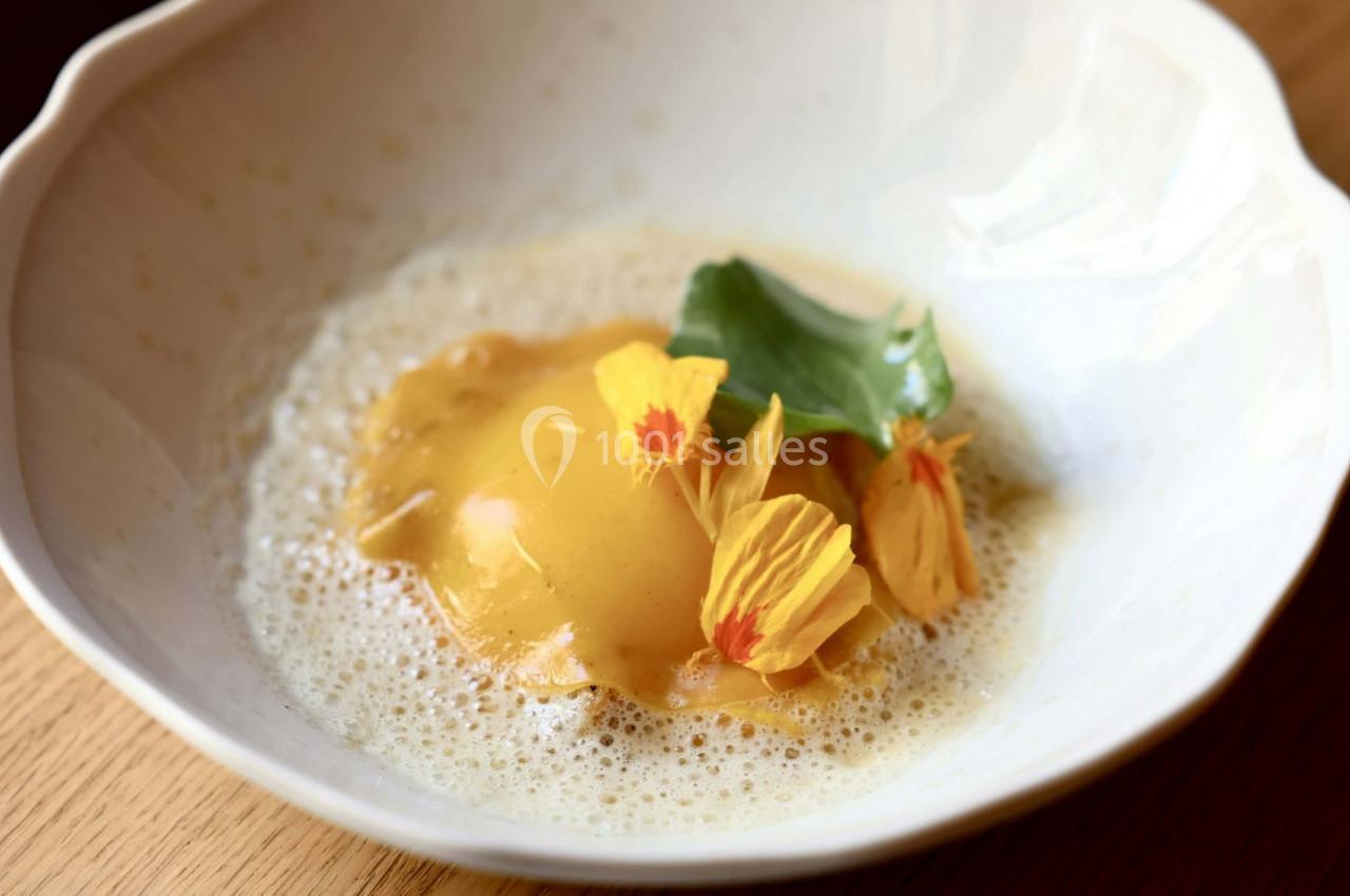 Ravioli garni, nappé de sauce mousseuse, décoré de fleurs comestibles jaunes et d'une feuille verte dans une assiette…