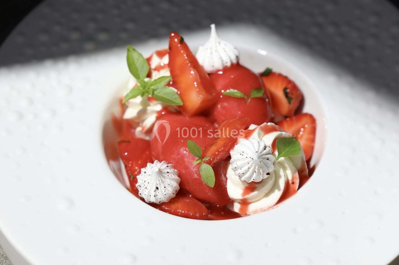 Dessert composé de fraises fraîches, sorbet, crème chantilly et petites feuilles de basilic dans une assiette blanche.