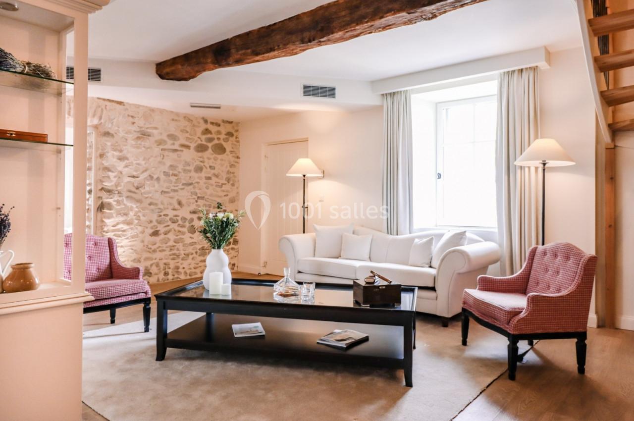 Salon lumineux avec canapé blanc, fauteuils roses, table basse en bois et mur en pierre apparente.