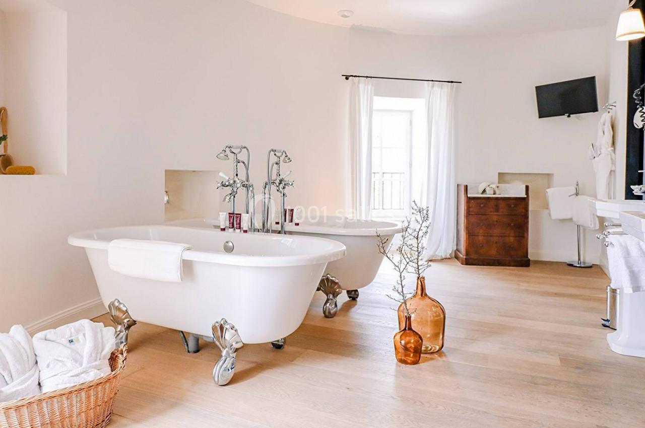 Salle de bain lumineuse avec deux baignoires sur pieds, parquet en bois clair et décoration minimaliste.
