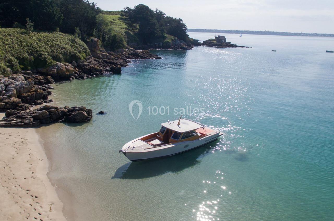 Bateau amarré près d'une plage de sable, entouré d'eau turquoise et de végétation côtière.