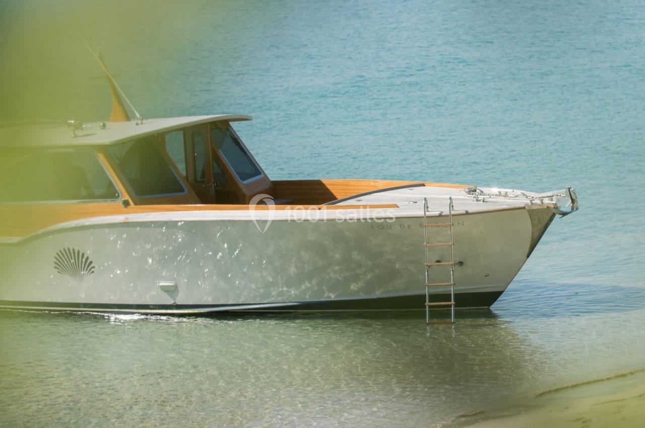 Bateau en bois et métal amarré dans une eau turquoise, avec une échelle accrochée à la proue.