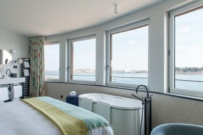 Chambre lumineuse avec lit double, bureau en bois, lampe et rideaux colorés près de fenêtres donnant sur l'extérieur.