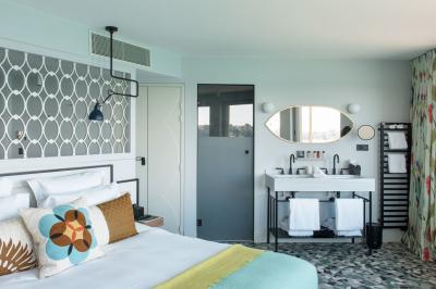 Chambre lumineuse avec lit double, bureau en bois, lampe et rideaux colorés près de fenêtres donnant sur l'extérieur.