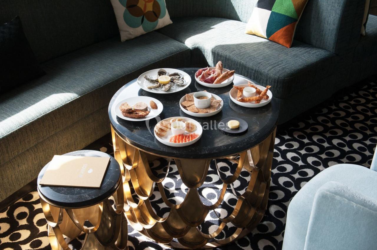 Table basse ronde avec petit-déjeuner varié, comprenant viennoiseries, fruits et boissons, dans un salon lumineux.
