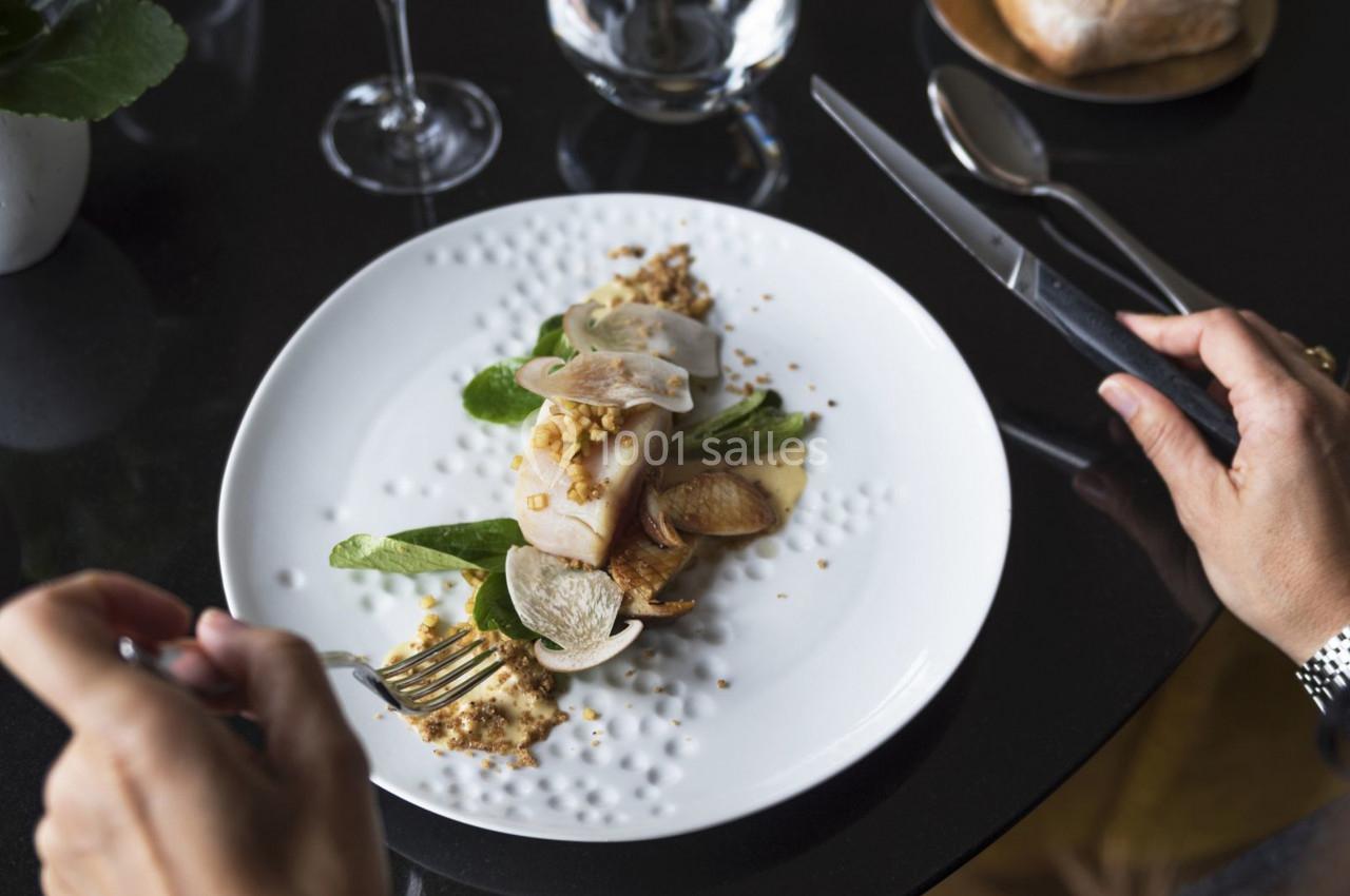 Assiette gastronomique avec viande, légumes verts, chips et sauce, sur une table noire, vue en cours de dégustation.