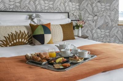 Chambre lumineuse avec lit double, bureau en bois, lampe et rideaux colorés près de fenêtres donnant sur l'extérieur.